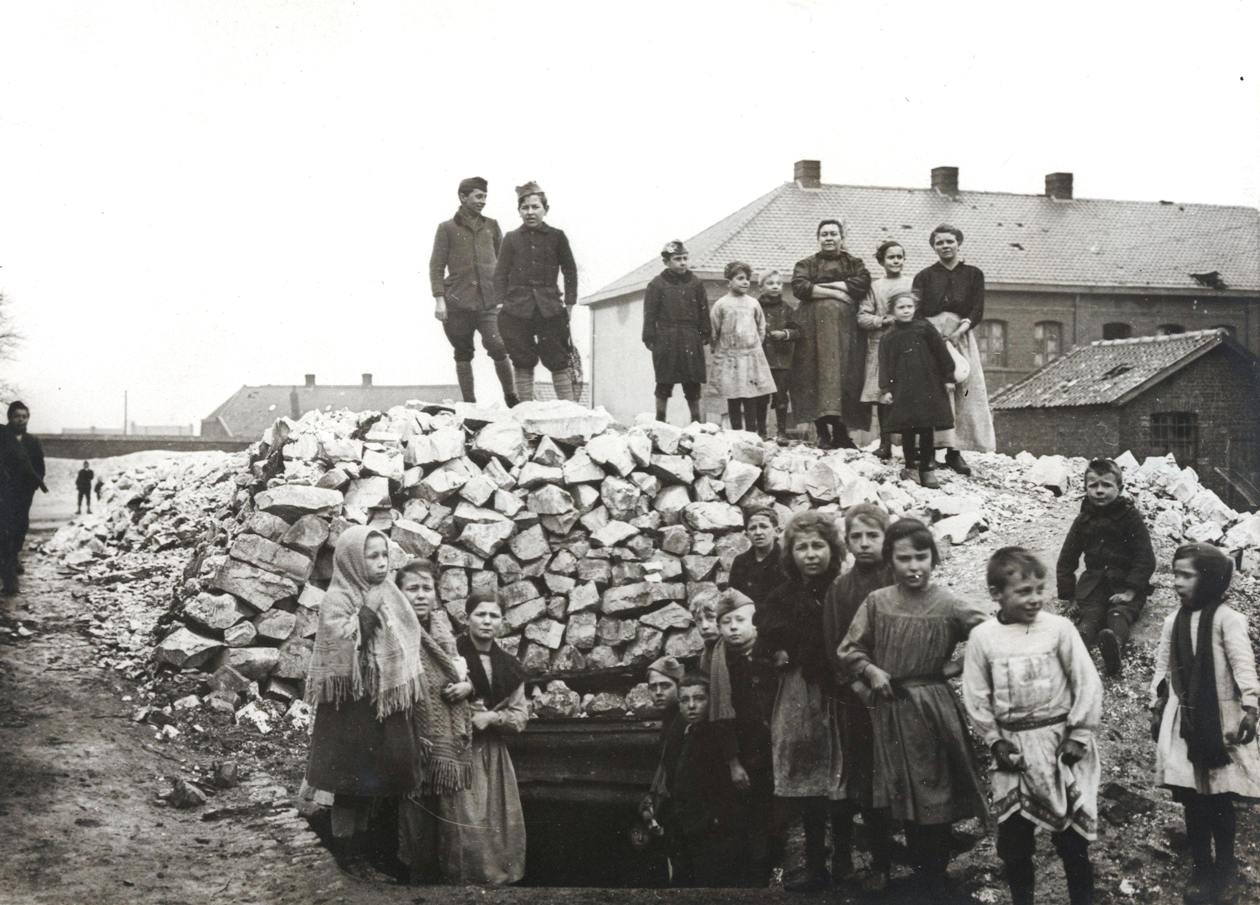 Photographie noir et blanc montrant des femmes et des enfants rassemblés autour d'un abri extérieur fait de sacs de jute.