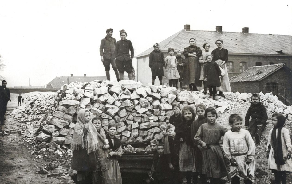 Photographie noir et blanc montrant des femmes et des enfants rassemblés autour d'un abri extérieur fait de sacs de jute.