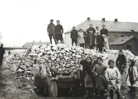 Photographie noir et blanc montrant des femmes et des enfants rassemblés autour d'un abri extérieur fait de sacs de jute.