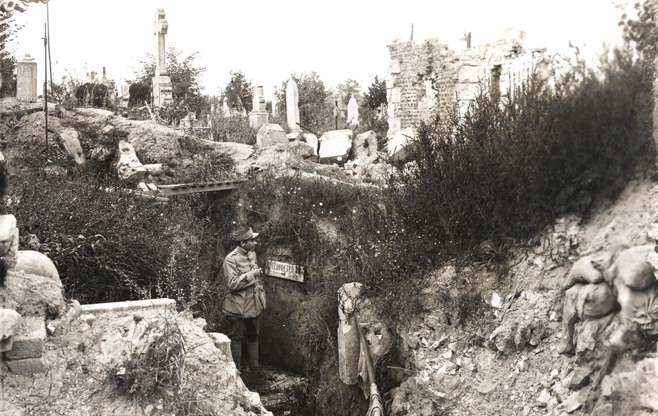 Photographie noir et blanc montrant un homme dans une tranchée surplombée par un cimetière.