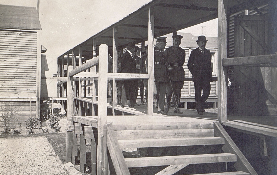 Photographie noir et blanc montrant un groupe d'hommes marchant sous un péristyle en bois.