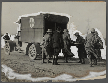 Photographie noir et blanc montrant des infirmiers casqués mettant une civière dans une camionette portant comme logo une croix.