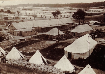 Photographie noir et blanc montrant un camp de tentes et de baraquements en bois.
