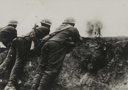 Photographie noir et blanc montrant trois soldats de dos, accoudés à un parapet. Au second plan, des explosions dues à un bombardement.