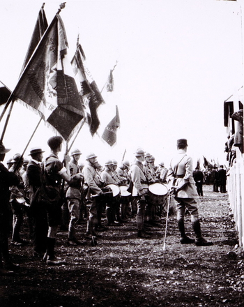 Photographie noir et blanc montrant une cérémonie militaire avec fanfare et drapeaux.
