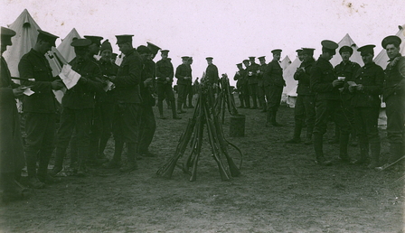 Photographie noir et blanc montrant un groupe de soldats britanniques devant des tentes, tenant des lettre à la main.