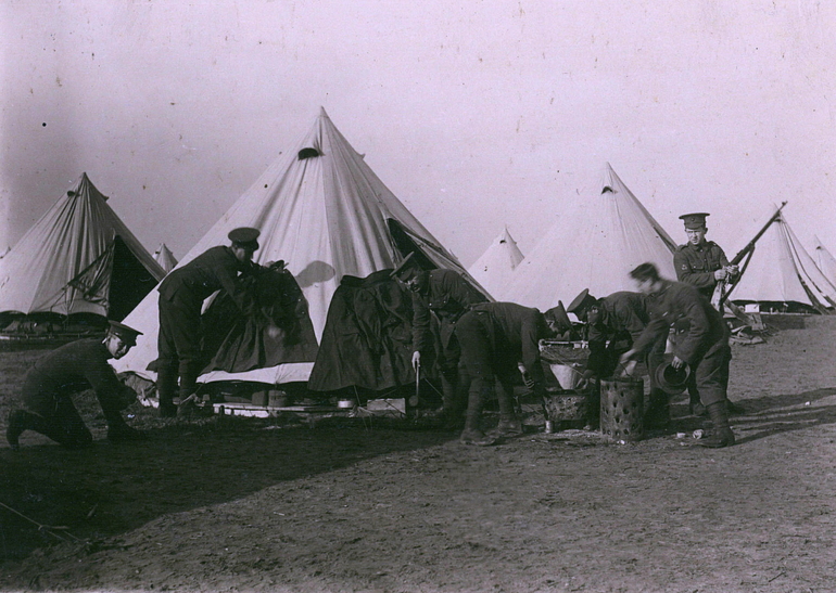 Photographie noir et blanc montrant des soldats s'affairant devant des tentes.
