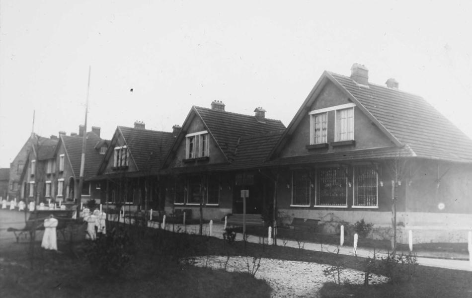 Photographie noir et blanc montrant une rue de maisons identiques, bordée par des jardins.