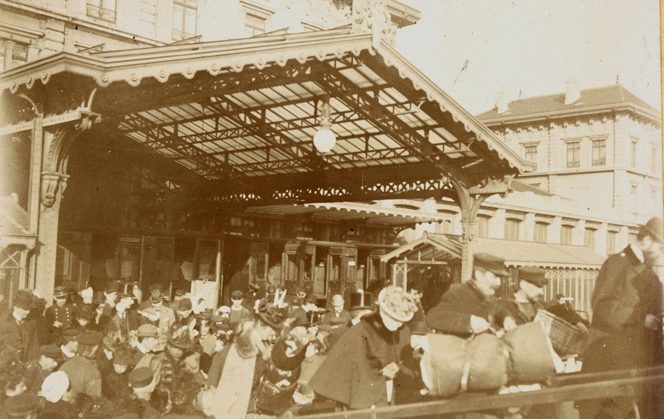 Photographie noir et blanc montrant le quai d'une gare rempli de voyageurs chargés de bagages.