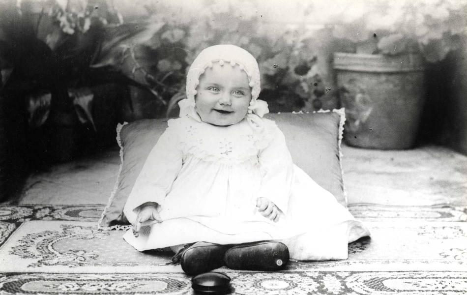 Photographie noir et blanc montrant un nourrisson assis sur un coussin.