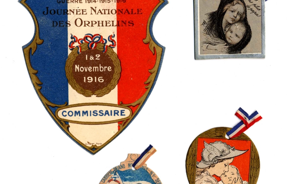 Quatre insignes colorés. Le premier est aux couleurs du drapeau français avec l'inscription : "Guerre 1914-1915-1916. Journée nationale des orphelins, 1 et 2 novembre 1916, commissaire". Le second montre deux enfants enlacés sous la légende : "Nous n'avons plus de papa !". Sur le troisième, un jeune garçon tient un drapeau français avec cette inscription "Journée des orphelins 1916. Nous entrerons dans la carrière quand nous n'y serons plus". Enfin, le dernier insigne est l'effigie d'une femme portant un casque ailé et serrant un nouvea-né contre elle".