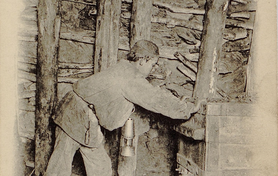 Carte postale noir et blanc montrant un jeunegarçon poussant un wagonnet dans une galerie de mine.