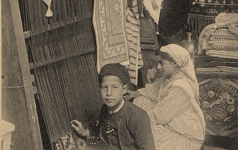 Carte postale noir et blanc montrant deux enfants en habit traditionnel arabe œuvrant sur un métier à tisser.