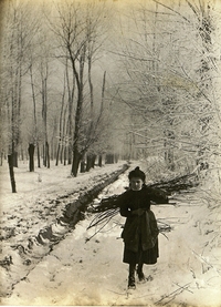 Photographie noir et blanc montrant une fillette portant un fagot de bois dans un paysage enneigé.