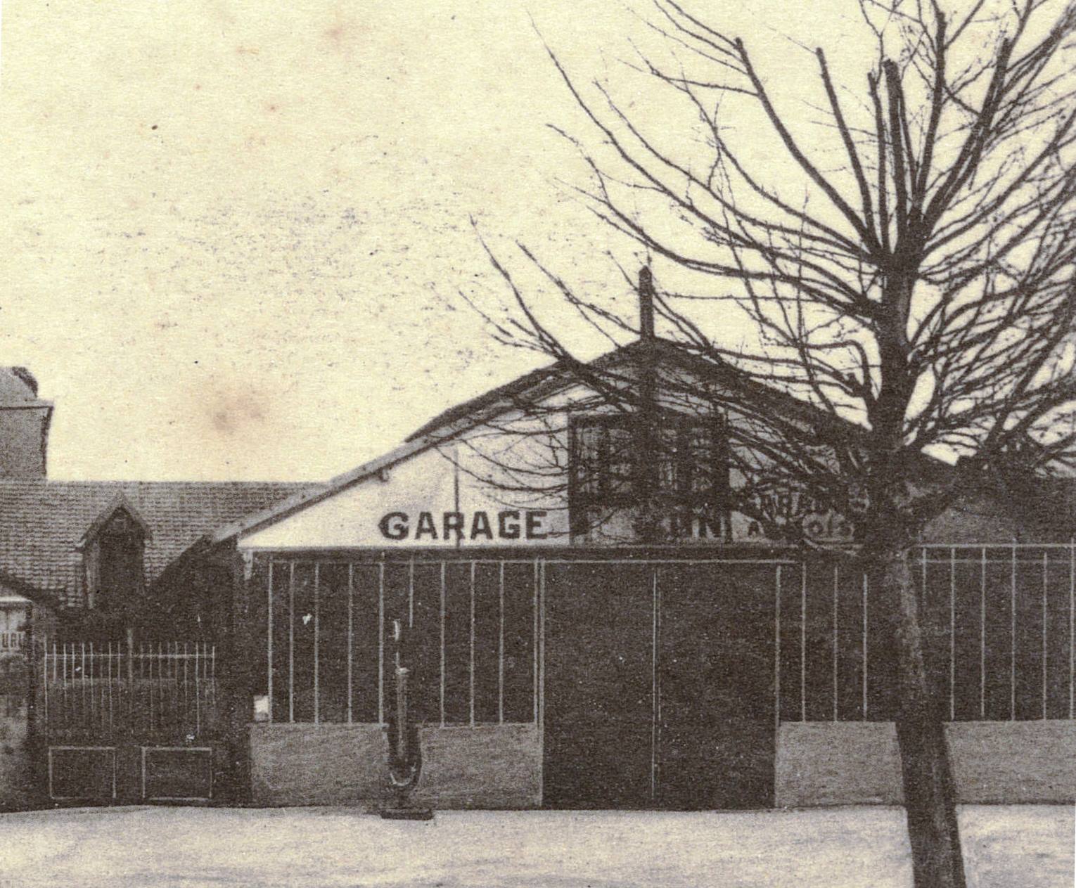 Photographie noir et blanc montrant un garage avec une pompe à essence.