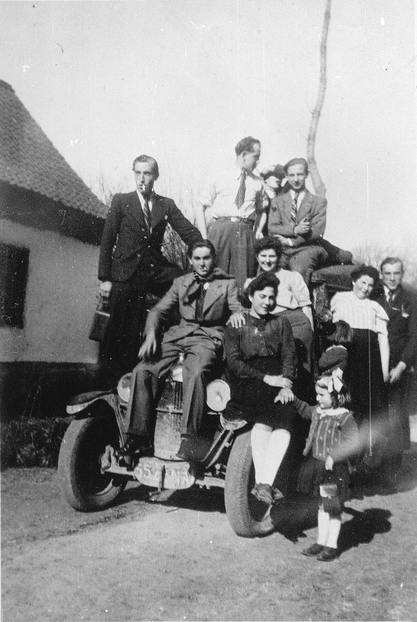 Photographie noir et blanc montrant un groupe de personnes devant et sur une voiture.