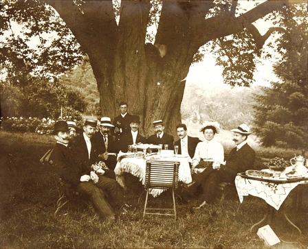 Photographie noir et blanc montrant un groupe de personnes déjeunant sous un arbre.