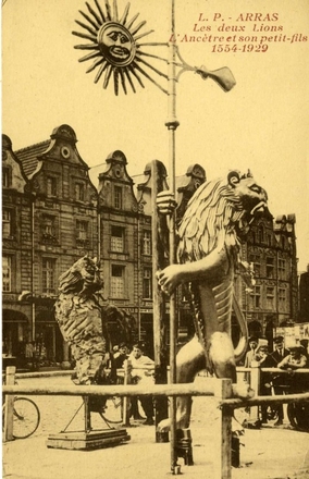 Carte postale noir et blanc sur fond jaune montrant au premier plan la statue d'un lion debout sur ses pattes arrières, tenant un mât au bout duquel sont accrochés une bannière et un soleil. Derrière lui se trouvent une autre statue érodée et des passants sur la place d'Arras.