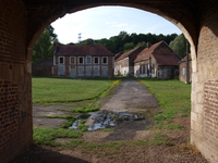 Photographie couleur montrant une porte cochère au premier pan qui donne sur des bâtiments similaires décrépis.