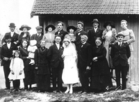 Photographie noir et blanc montrant un couple de jeunes mariés entourés de leur famille.