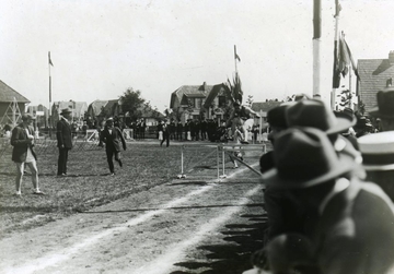 Photographie noir et blanc d'un athlète sautant une haie, encouragé par les spectateurs le regardant du bas-côté.