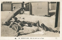 Carte postale noir et blanc montrant un groupe de personnes allongées sur la plage, devant des cabanons de plage.