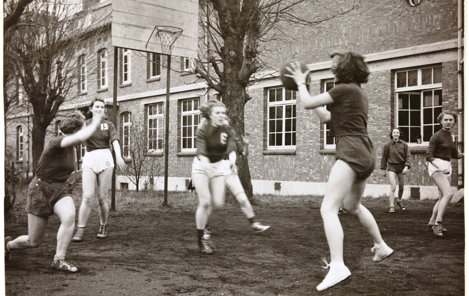 Photographie noir et blanc montrant des jeunes filles jouant au basket ball en tenue de sport.