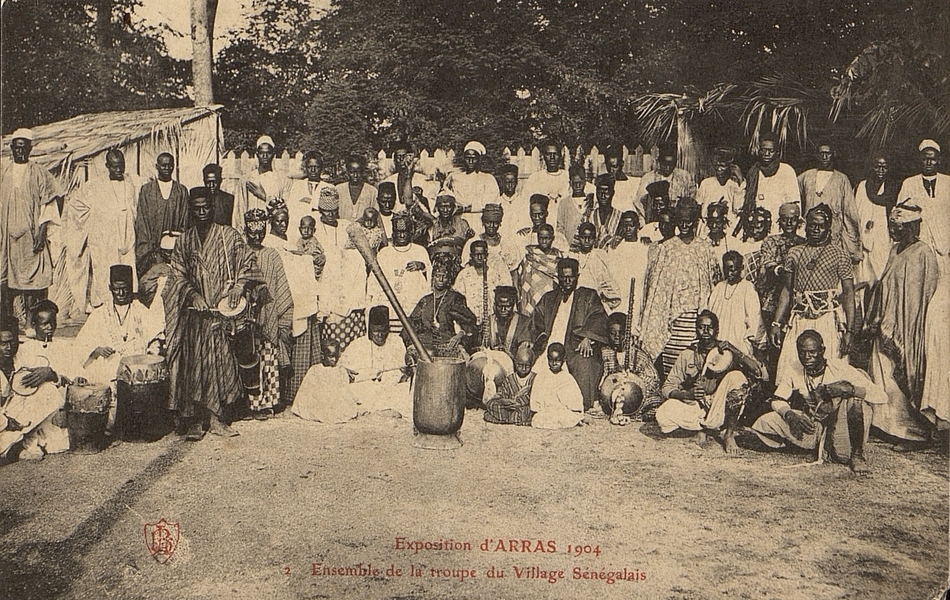 Groupe d'une cinquantaine de sénégalais regroupés assis et debouts sur plusieurs rangées. Ils portent des habits traditionnels et posent avec des instruments de musique.