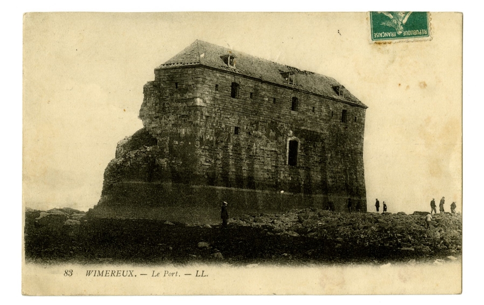 Carte postale en noir et blanc d’un grand bâtiment délabré dans les rochers, à marée basse. Autour, quelques promeneurs