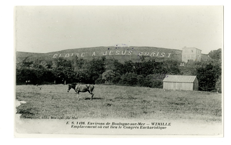 Carte postale en noir et blanc d’une pâture à Wimille. Au premier plan, un cheval et un hangar. Sur une colline derrière, on lit l’inscription "Gloire à Jésus-Christ" posée à l’occasion du congrès eucharistique de 1892