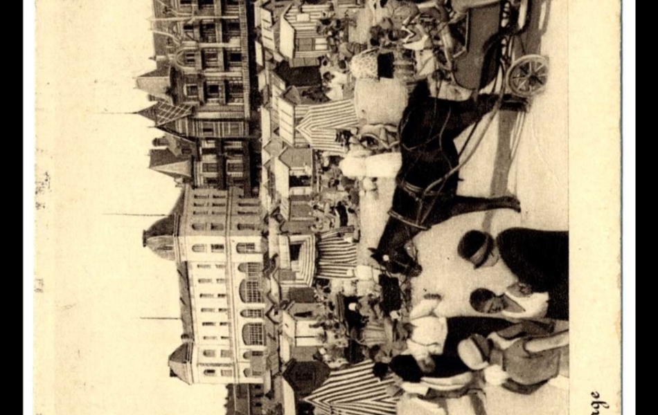 Photographie noir et blanc d’une scène de plage. On voit en arrière-plan des villas de style normand et le casino en pierre blanche.  Au premier plan, un âne tire une calèche. De nombreuses cabines et des tentes recouvrent la plage noire de monde. D’après les costumes, on imagine que la scène se passe dans les années 30-40. 