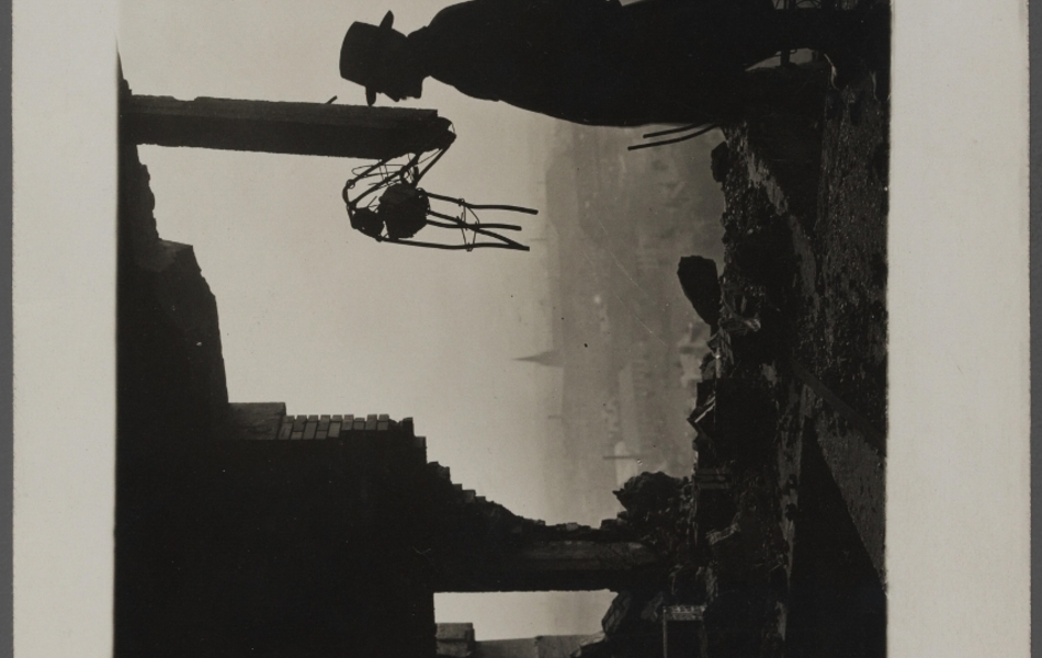 Photographie noir et blanc montrant la silhouette d'un homme de profil portant un chapeau, sur la partie supérieure de la tour atteinte par une bombe.