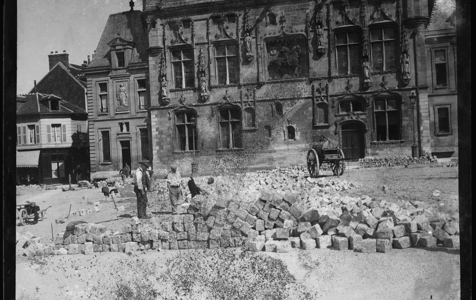 Photographie noire et blanc montrant des ouvriers œuvrant sur une place pavée.