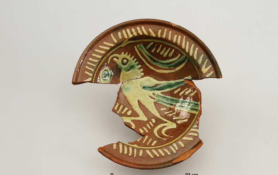 Photo d’une écuelle partiellement recomposée de plusieurs fragments. Le décor est un oiseau.
